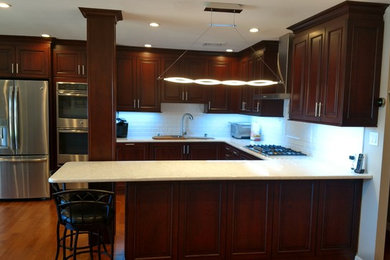 Inspiration for a large transitional u-shaped medium tone wood floor kitchen remodel in New York with an undermount sink, raised-panel cabinets, dark wood cabinets, white backsplash, subway tile backsplash, stainless steel appliances and a peninsula