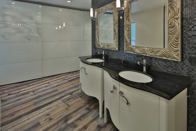Large minimalist master white tile and ceramic tile medium tone wood floor and multicolored floor bathroom photo in Sacramento with furniture-like cabinets, white cabinets, a one-piece toilet, white walls, an undermount sink, quartz countertops and black countertops