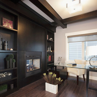Klassisk inredning av ett hemmabibliotek, med grå väggar, mörkt trägolv, en dubbelsidig öppen spis, en spiselkrans i trä och ett fristående skrivbord