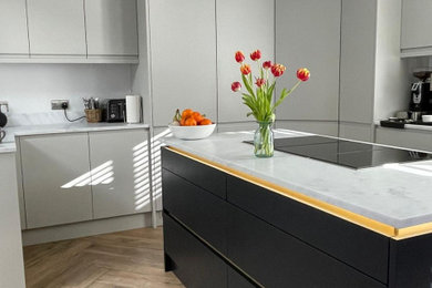 This is an example of a modern grey and black l-shaped open plan kitchen in Essex with a submerged sink, flat-panel cabinets, grey cabinets, composite countertops, white splashback, integrated appliances, porcelain flooring, an island, brown floors, white worktops, a drop ceiling and feature lighting.