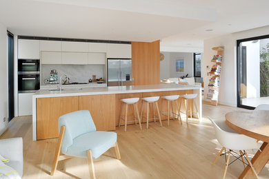 This is an example of a mid-sized modern galley eat-in kitchen in Sydney with light wood cabinets, solid surface benchtops, stone slab splashback, stainless steel appliances, light hardwood floors and with island.