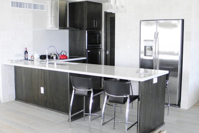Small zen l-shaped light wood floor and gray floor eat-in kitchen photo in Hawaii with an undermount sink, flat-panel cabinets, black cabinets, solid surface countertops, gray backsplash, ceramic backsplash, stainless steel appliances and a peninsula