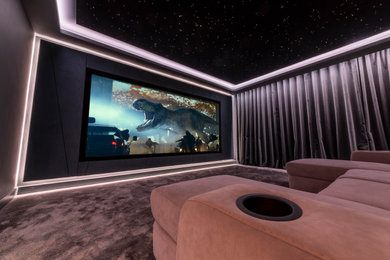 Photo of a medium sized enclosed home cinema in Kent with grey walls, carpet, a projector screen, grey floors and a feature wall.