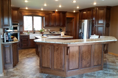Large elegant u-shaped ceramic tile kitchen photo in Other with a farmhouse sink, raised-panel cabinets, medium tone wood cabinets, granite countertops, stainless steel appliances and two islands