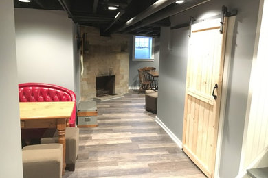 Cette image montre une salle de séjour design de taille moyenne et ouverte avec une salle de musique, un mur gris, un sol en bois brun, une cheminée standard, un manteau de cheminée en pierre, un téléviseur fixé au mur et un sol marron.