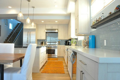 Mid-sized beach style l-shaped light wood floor enclosed kitchen photo in Los Angeles with an undermount sink, shaker cabinets, white cabinets, quartz countertops, gray backsplash, ceramic backsplash, stainless steel appliances and an island