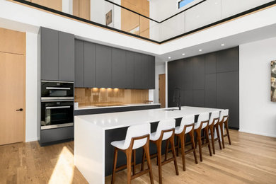 Open concept kitchen - mid-sized l-shaped medium tone wood floor and brown floor open concept kitchen idea in Nashville with a double-bowl sink, flat-panel cabinets, gray cabinets, quartz countertops, brown backsplash, wood backsplash, stainless steel appliances, an island and white countertops