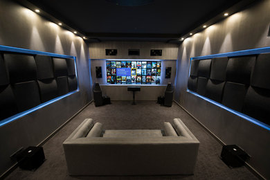 Ejemplo de cine en casa cerrado moderno de tamaño medio con paredes grises, moqueta, televisor colgado en la pared y suelo gris