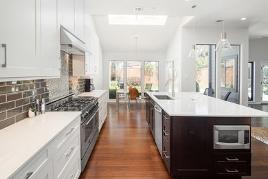 Example of a large transitional single-wall bamboo floor and brown floor open concept kitchen design in Dallas with an undermount sink, flat-panel cabinets, white cabinets, quartz countertops, gray backsplash, glass tile backsplash, stainless steel appliances, an island and white countertops