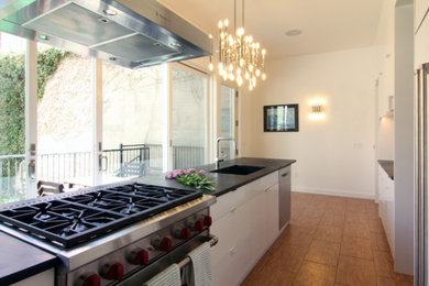 Example of a mid-sized minimalist galley cork floor kitchen design in New York with an integrated sink, flat-panel cabinets, white cabinets, soapstone countertops, blue backsplash, ceramic backsplash, stainless steel appliances and an island