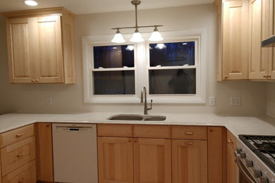 Example of a mid-sized classic u-shaped kitchen design in Burlington with raised-panel cabinets, light wood cabinets, quartz countertops and white appliances