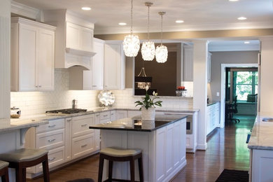 Inspiration for a large transitional u-shaped medium tone wood floor eat-in kitchen remodel in Cincinnati with a farmhouse sink, recessed-panel cabinets, white cabinets, granite countertops, white backsplash, subway tile backsplash, paneled appliances and two islands