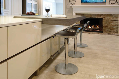 Example of a trendy porcelain tile kitchen design in Cleveland with an undermount sink, flat-panel cabinets, beige cabinets, quartz countertops, beige backsplash, glass sheet backsplash, stainless steel appliances and an island