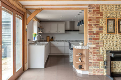 Mid-sized modern l-shaped open plan kitchen in Sussex with an undermount sink, shaker cabinets, white cabinets, quartzite benchtops, white splashback, black appliances, ceramic floors, with island, beige floor, grey benchtop and exposed beam.