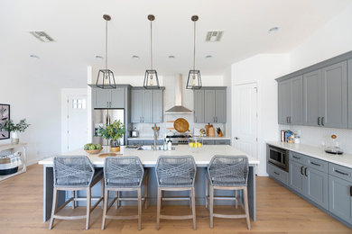 Example of a large cottage l-shaped light wood floor open concept kitchen design in Phoenix with an undermount sink, shaker cabinets, gray cabinets, quartz countertops, white backsplash, porcelain backsplash, stainless steel appliances, an island and white countertops