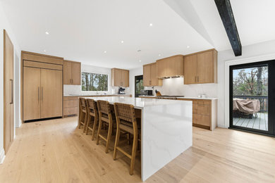 Example of a mid-sized minimalist l-shaped light wood floor, brown floor and exposed beam open concept kitchen design in Atlanta with an undermount sink, flat-panel cabinets, light wood cabinets, quartz countertops, white backsplash, quartz backsplash, stainless steel appliances, an island and white countertops
