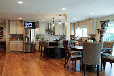 Example of a mid-sized classic l-shaped medium tone wood floor open concept kitchen design in Columbus with raised-panel cabinets, white cabinets, granite countertops, beige backsplash, stone tile backsplash, stainless steel appliances, an island and a farmhouse sink