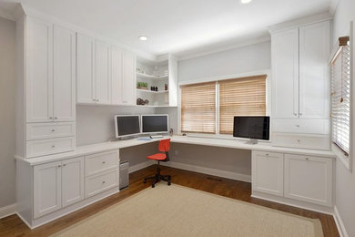 This is an example of a large modern home office in Philadelphia with white walls, medium hardwood floors, a built-in desk and brown floor.
