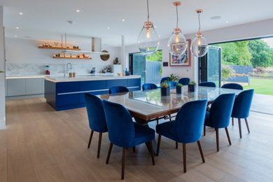 This is an example of a large modern l-shaped kitchen/diner in Berkshire with a built-in sink, flat-panel cabinets, blue cabinets, quartz worktops, white splashback, stainless steel appliances, medium hardwood flooring, an island, brown floors and white worktops.