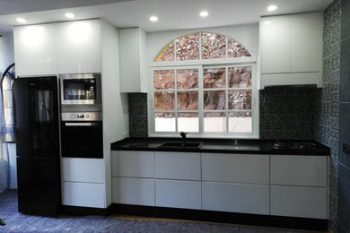 Modelo de cocina minimalista con armarios con paneles lisos, puertas de armario blancas y encimeras negras
