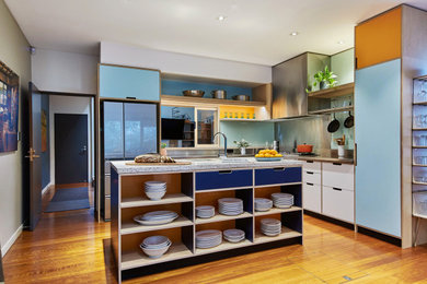 This is an example of a mid-sized contemporary l-shaped open plan kitchen in Sydney with an undermount sink, stainless steel benchtops, green splashback, glass sheet splashback, stainless steel appliances, with island, flat-panel cabinets, blue cabinets, medium hardwood floors, brown floor and grey benchtop.