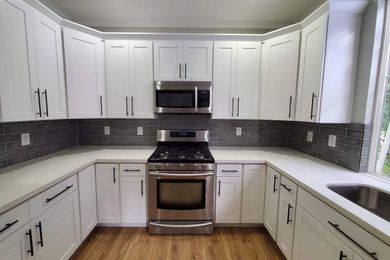 Example of an u-shaped laminate floor and brown floor eat-in kitchen design in Seattle with a drop-in sink, shaker cabinets, gray backsplash, ceramic backsplash, stainless steel appliances, no island and white countertops