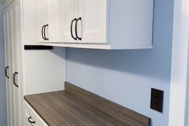 ワシントンD.C.にある高級な中くらいなシャビーシック調のおしゃれな洗濯室 (ll型、エプロンフロントシンク、インセット扉のキャビネット、白いキャビネット、ラミネートカウンター、青いキッチンパネル、セラミックタイルのキッチンパネル、青い壁、ラミネートの床、左右配置の洗濯機・乾燥機、茶色い床、グレーのキッチンカウンター) の写真