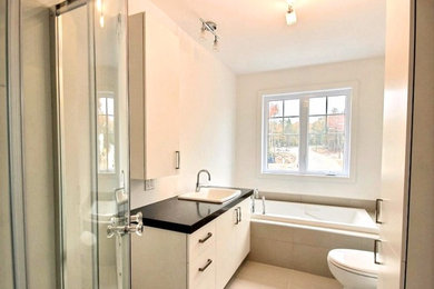 Inspiration for a mid-sized contemporary master beige tile and ceramic tile ceramic tile and beige floor bathroom remodel in Other with flat-panel cabinets, white cabinets, a one-piece toilet, white walls, a drop-in sink, solid surface countertops and black countertops
