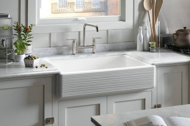 Example of a transitional l-shaped eat-in kitchen design in Providence with a farmhouse sink, recessed-panel cabinets, white cabinets, solid surface countertops, white backsplash, ceramic backsplash and an island