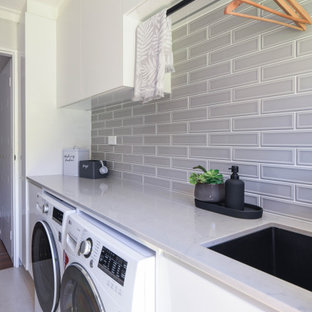 Foto di una sala lavanderia moderna di medie dimensioni con lavello sottopiano, ante lisce, ante bianche, top in quarzo composito, paraspruzzi grigio, paraspruzzi con piastrelle in ceramica, pareti bianche, pavimento con piastrelle in ceramica, lavatrice e asciugatrice affiancate, pavimento beige e top grigio