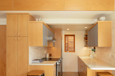 Example of a mid-sized danish galley cork floor eat-in kitchen design in San Luis Obispo with an undermount sink, flat-panel cabinets, light wood cabinets, solid surface countertops, white backsplash, stainless steel appliances, white countertops and subway tile backsplash