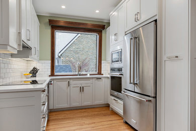 Open concept kitchen - small mid-century modern u-shaped light wood floor and brown floor open concept kitchen idea in Other with an undermount sink, shaker cabinets, beige cabinets, quartz countertops, white backsplash, subway tile backsplash, stainless steel appliances, an island and white countertops