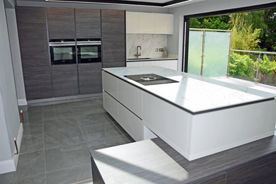 Large modern single-wall open plan kitchen in Essex with with island, an undermount sink, flat-panel cabinets, white splashback, porcelain splashback, panelled appliances, porcelain floors, grey floor and white benchtop.