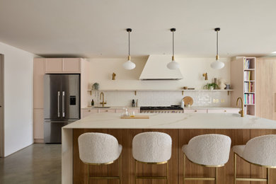 Photo of an expansive scandinavian grey and pink galley open plan kitchen in London with an integrated sink, shaker cabinets, pink cabinets, composite countertops, white splashback, ceramic splashback, stainless steel appliances, concrete flooring, an island, grey floors, white worktops and feature lighting.