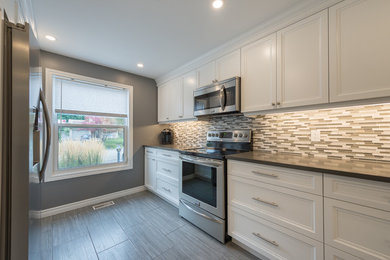 Enclosed kitchen - mid-sized transitional galley enclosed kitchen idea in Toronto with recessed-panel cabinets, white cabinets, gray backsplash and stainless steel appliances