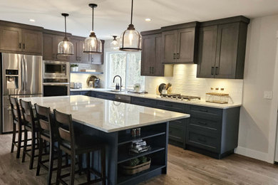 Large cottage l-shaped laminate floor and brown floor open concept kitchen photo in Vancouver with an undermount sink, shaker cabinets, medium tone wood cabinets, quartz countertops, white backsplash, porcelain backsplash, stainless steel appliances, an island and white countertops