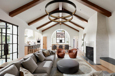 Example of a large tuscan medium tone wood floor, brown floor and vaulted ceiling living room design in San Francisco with white walls, a standard fireplace and a plaster fireplace