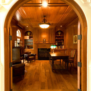 Bild på ett stort vintage arbetsrum, med ett bibliotek, bruna väggar, mörkt trägolv, en standard öppen spis, en spiselkrans i trä, ett fristående skrivbord och brunt golv