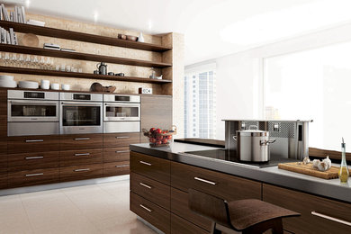 Kitchen - large contemporary single-wall porcelain tile kitchen idea in Vancouver with flat-panel cabinets, dark wood cabinets, solid surface countertops, beige backsplash, stone tile backsplash, stainless steel appliances and an island