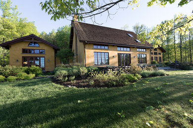 Large mountain style yellow two-story stucco house exterior photo in Other with a hip roof and a shingle roof