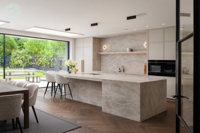 Photo of a large modern grey and brown single-wall kitchen/diner in Berkshire with a built-in sink, beige cabinets, marble worktops, marble splashback, medium hardwood flooring, a breakfast bar, brown floors and feature lighting.