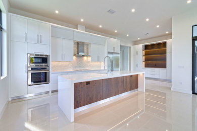 Example of a large minimalist galley kitchen pantry design in Miami with flat-panel cabinets, white cabinets, quartzite countertops, gray backsplash, glass sheet backsplash and an island