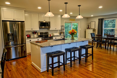 Design ideas for an expansive country eat-in kitchen in DC Metro with an undermount sink, white cabinets, granite benchtops, white splashback, subway tile splashback, stainless steel appliances, medium hardwood floors, with island, brown floor and black benchtop.