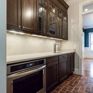 This is an example of a transitional single-wall kitchen pantry in DC Metro with an undermount sink, dark wood cabinets, white splashback, stainless steel appliances, brick floors, red floor and white benchtop.