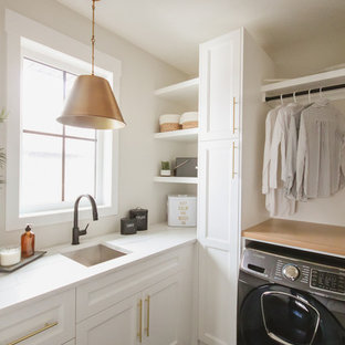 Photo of a classic l-shaped utility room in Other with a submerged sink, recessed-panel cabinets, white cabinets, white walls, a side by side washer and dryer, black floors and white worktops.