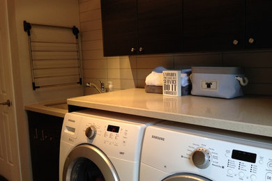 Dedicated laundry room - mid-sized contemporary single-wall porcelain tile dedicated laundry room idea in Toronto with a single-bowl sink, flat-panel cabinets, black cabinets, quartz countertops, gray walls and a side-by-side washer/dryer