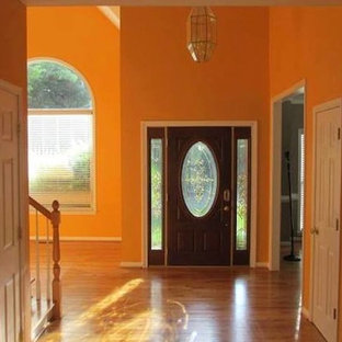 Idée de décoration pour une entrée bohème avec un couloir, un mur orange, un sol en bois clair, une porte simple et une porte en bois foncé.