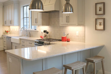 Example of a large transitional galley medium tone wood floor and brown floor enclosed kitchen design in Other with a farmhouse sink, shaker cabinets, gray cabinets, quartzite countertops, stainless steel appliances, beige backsplash, subway tile backsplash and a peninsula