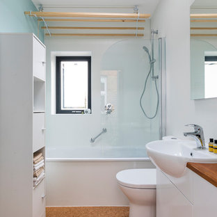 Réalisation d'une petite douche en alcôve design pour enfant avec un placard à porte plane, des portes de placard blanches, une baignoire en alcôve, un WC à poser, des plaques de verre, un mur blanc, un sol en liège, un lavabo posé, un plan de toilette en bois, un sol marron, une cabine de douche à porte battante et un plan de toilette marron.