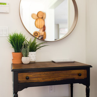 Inredning av en eklektisk liten foajé, med vita väggar, mellanmörkt trägolv, en enkeldörr, en svart dörr och brunt golv